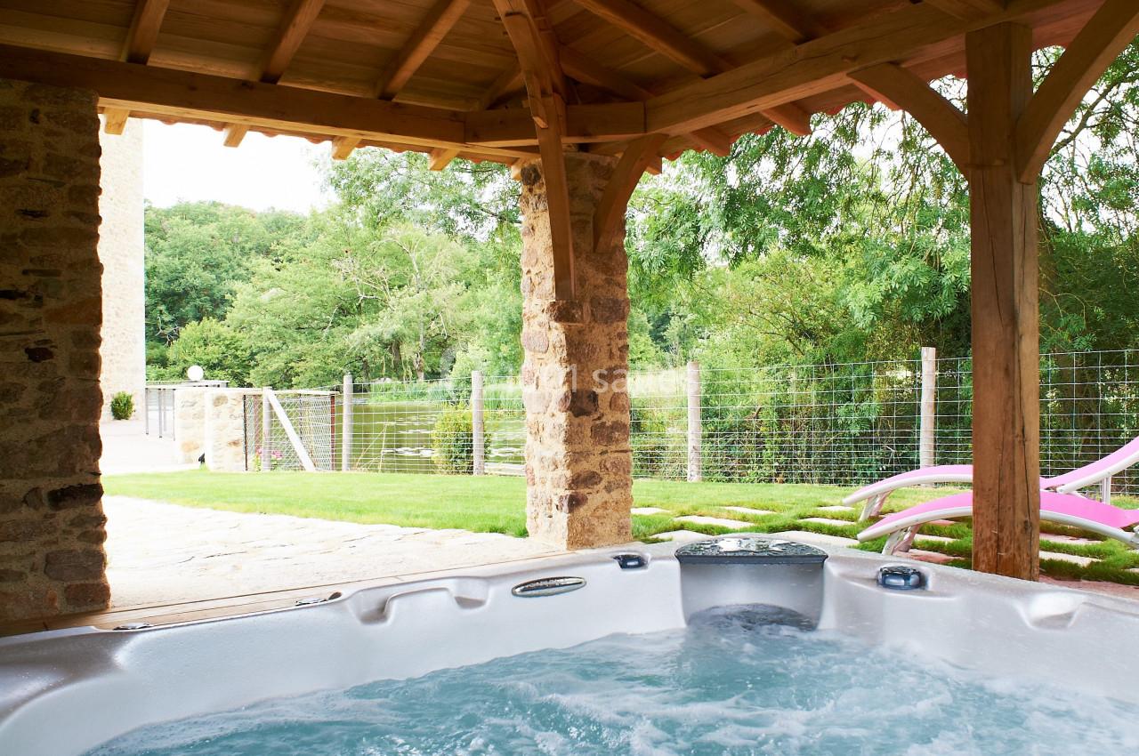 Vue d'un jacuzzi extérieur sous une pergola en bois, avec un jardin verdoyant en arrière-plan.