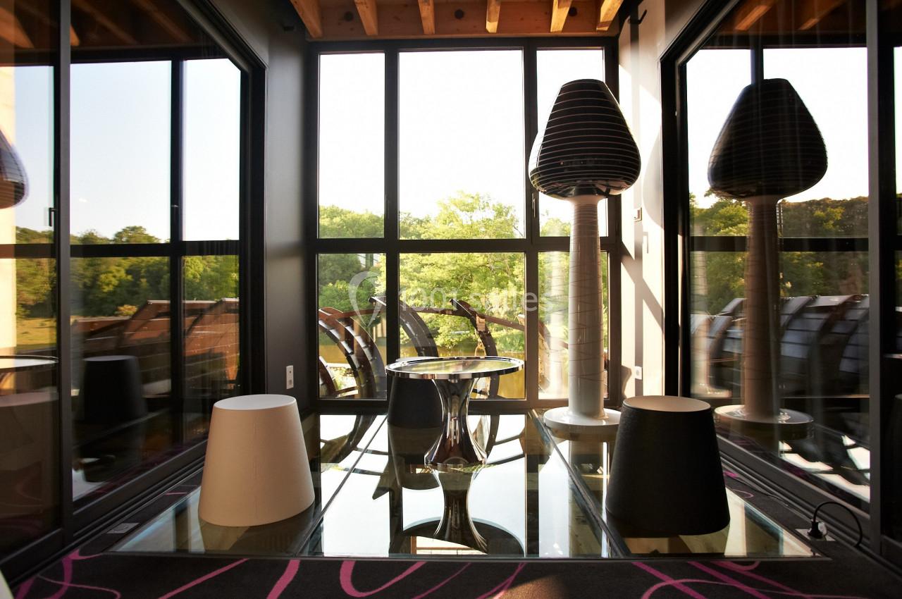 Espace lumineux avec grandes baies vitrées, mobilier design et vue sur un paysage verdoyant.