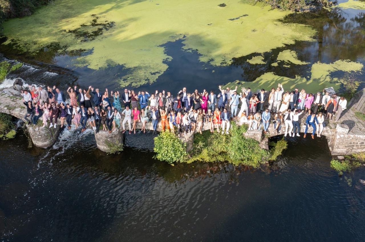 Un grand groupe de personnes debout sur un pont en pierre au-dessus d'une rivière entourée de végétation.
