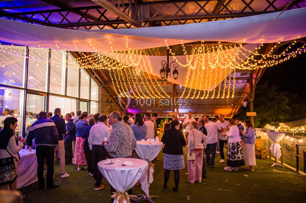 Groupe de personnes rassemblées sous une structure illuminée par des guirlandes lumineuses lors d'un événement en soirée.