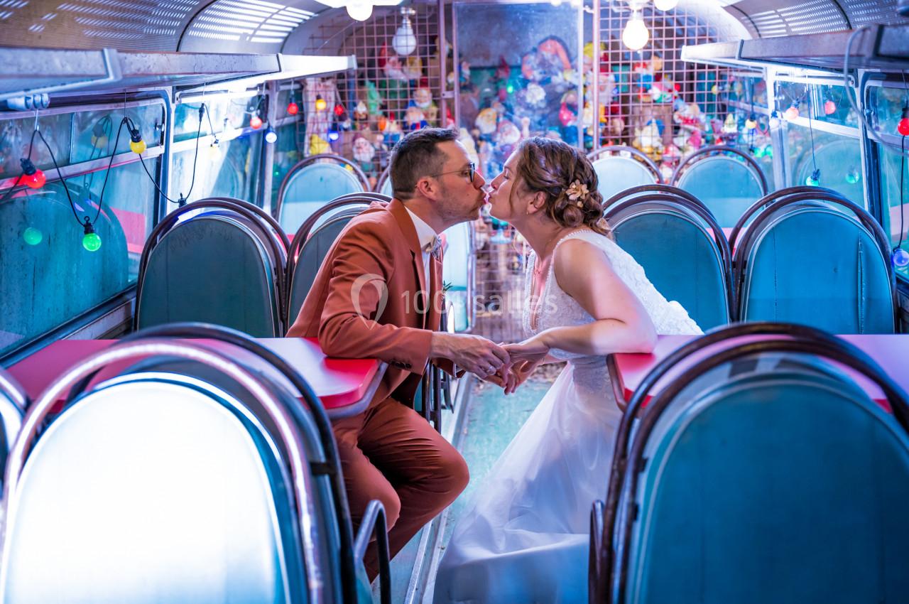 Un couple en tenue de mariage s'embrasse dans un décor coloré à l'intérieur d'un bus aménagé.