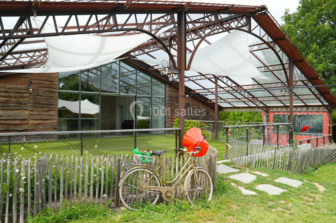 Vélo ancien garé devant une structure en bois et métal avec des toiles blanches tendues, entourée de verdure.