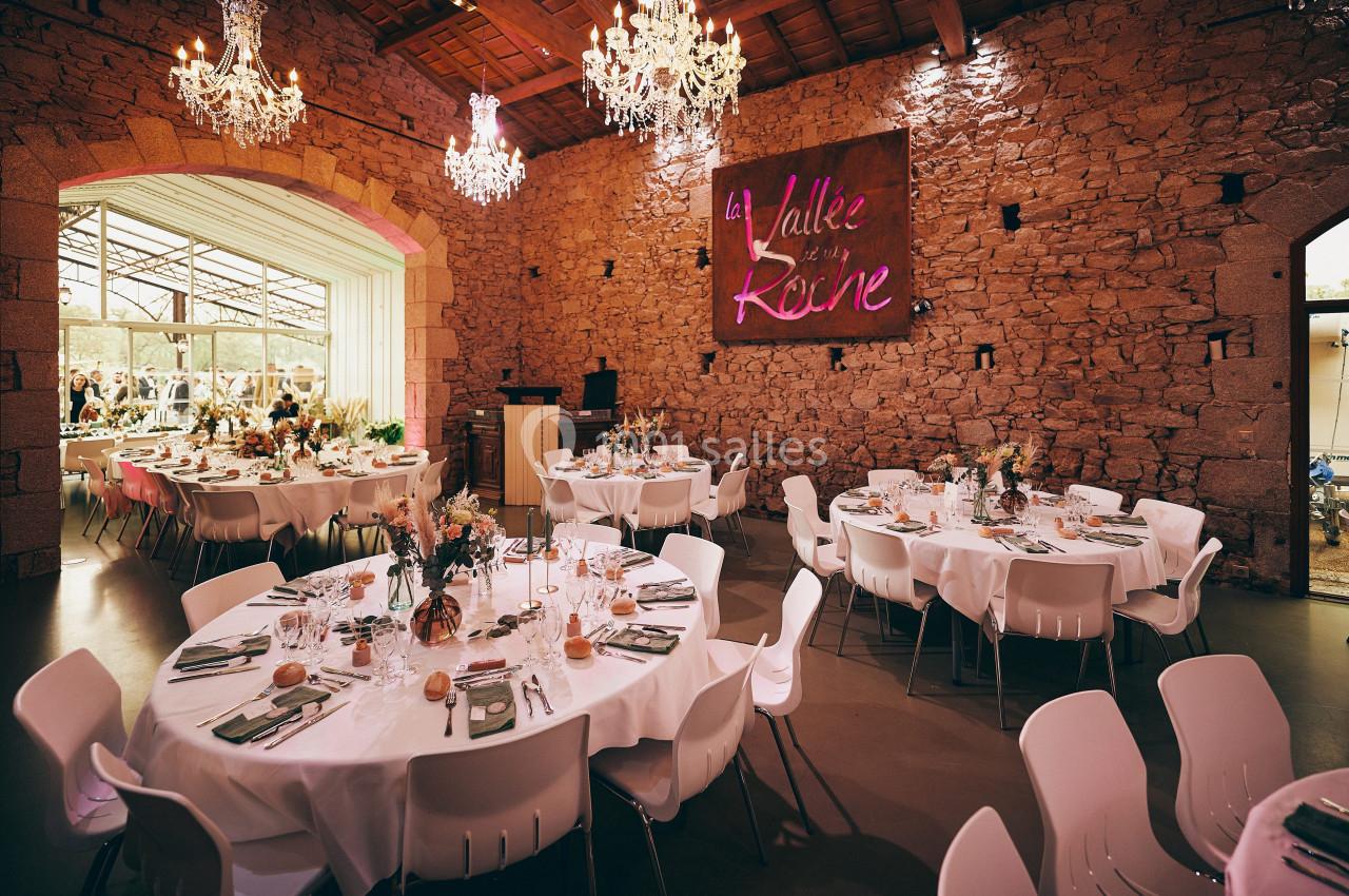 Salle de réception décorée avec des tables rondes dressées, des chaises blanches et des lustres suspendus.