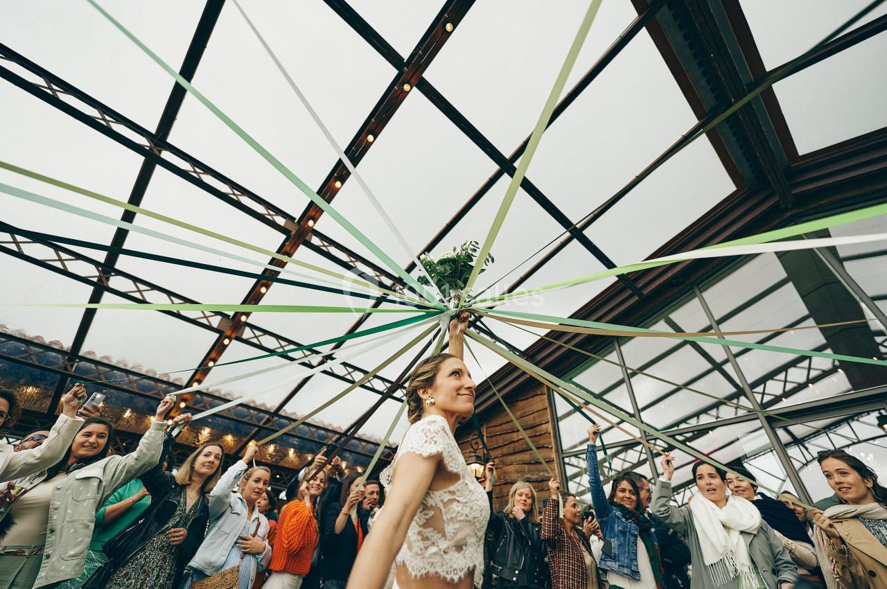 Une femme danse sous des rubans tendus, entourée d'invités dans une salle lumineuse avec une verrière.