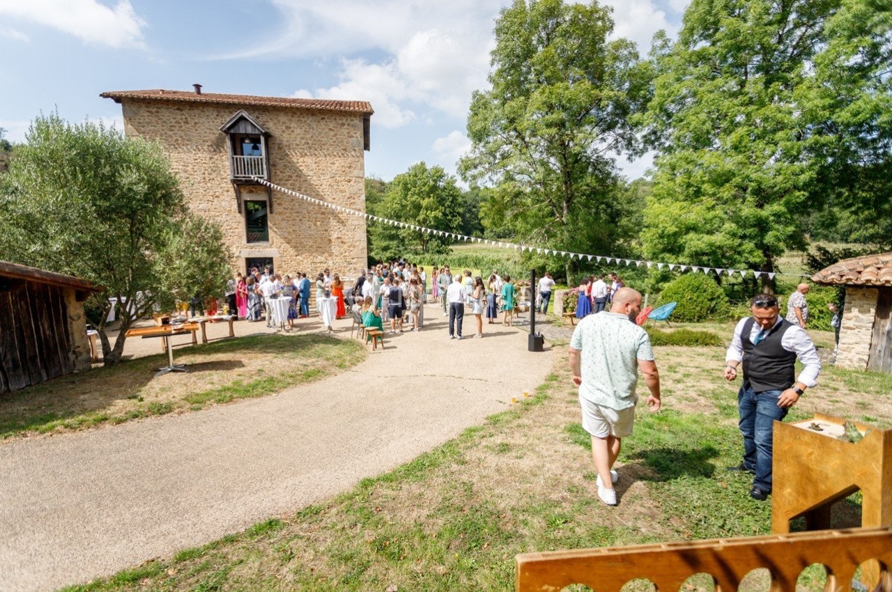 Groupe de personnes rassemblées dans une cour devant une maison en pierre, décorée pour un événement festif en plein air.