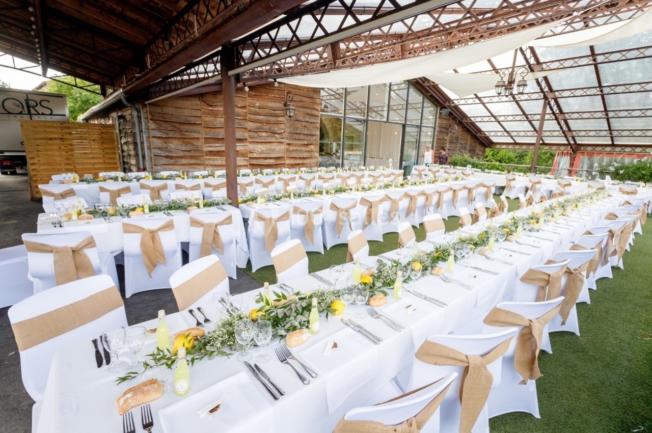 Tables alignées et décorées avec des nappes blanches, chemins de table en toile de jute et arrangements floraux jaunes et…