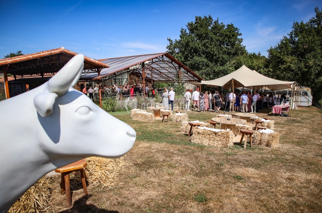 Statue de vache blanche au premier plan, avec des stands et des visiteurs dans un espace extérieur en arrière-plan.