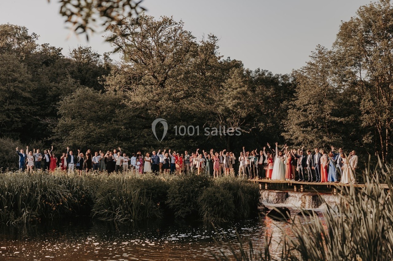 Un grand groupe de personnes posant sur un pont en bois, entouré de végétation et d'un plan d'eau.