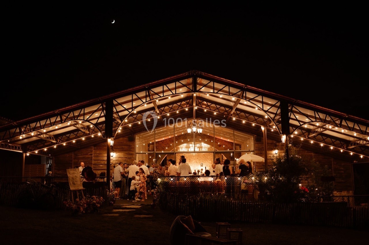 Salle en bois illuminée la nuit, avec des invités rassemblés pour un événement festif sous un ciel étoilé.