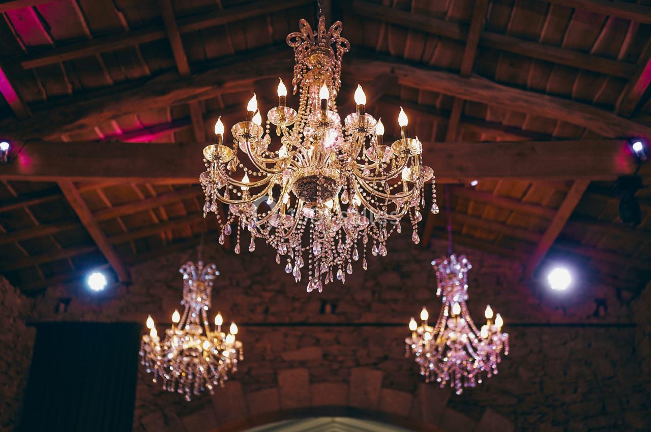 Trois lustres en cristal éclairés suspendus sous un plafond en bois dans une salle en pierre.