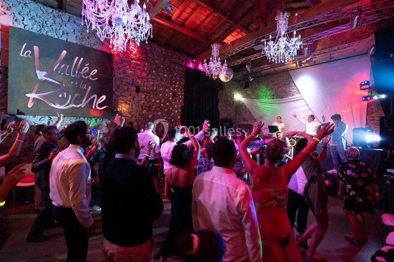Personnes dansant lors d'une soirée festive dans une salle en pierre avec des lustres et un éclairage coloré.