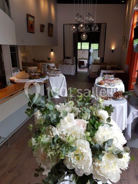 Salle élégante décorée pour un événement, avec des tables garnies de buffets et un bouquet de fleurs blanches au premier…