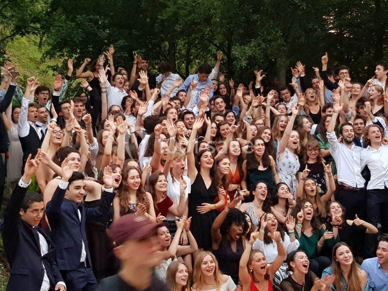 Groupe de jeunes adultes souriants levant les bras lors d'un rassemblement en extérieur devant des arbres.