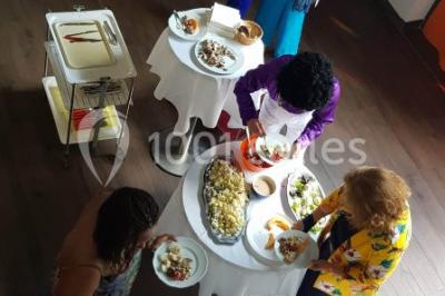 Des personnes se servent à un buffet varié disposé sur des tables rondes dans une salle lumineuse.