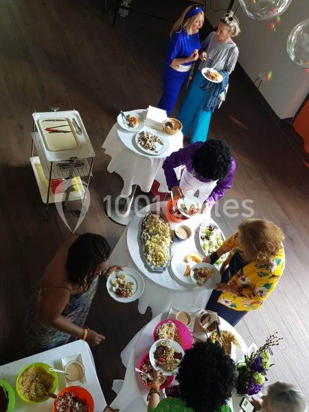 Des personnes se servent à un buffet varié disposé sur des tables rondes dans une salle lumineuse.