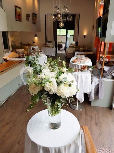 Salle décorée pour un événement avec des tables garnies de plats et un bouquet de fleurs blanches au premier plan.