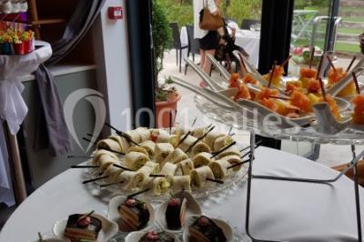 Buffet avec des plats variés, dont des salades, du saumon fumé et des fruits, décoré d'un bouquet de fleurs violettes et…