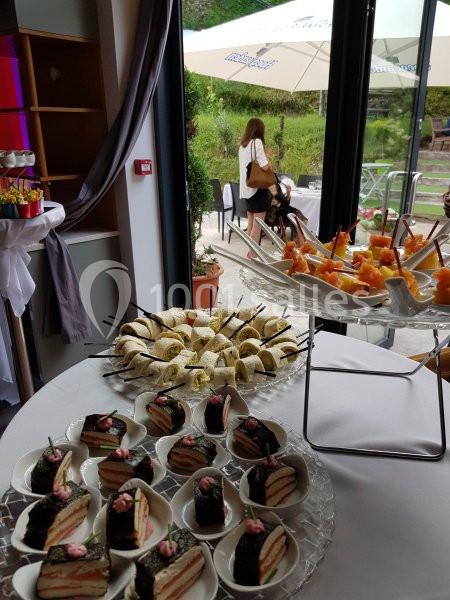 Buffet avec gâteaux, brochettes de fruits et sandwichs, disposé près d'une baie vitrée donnant sur un jardin.