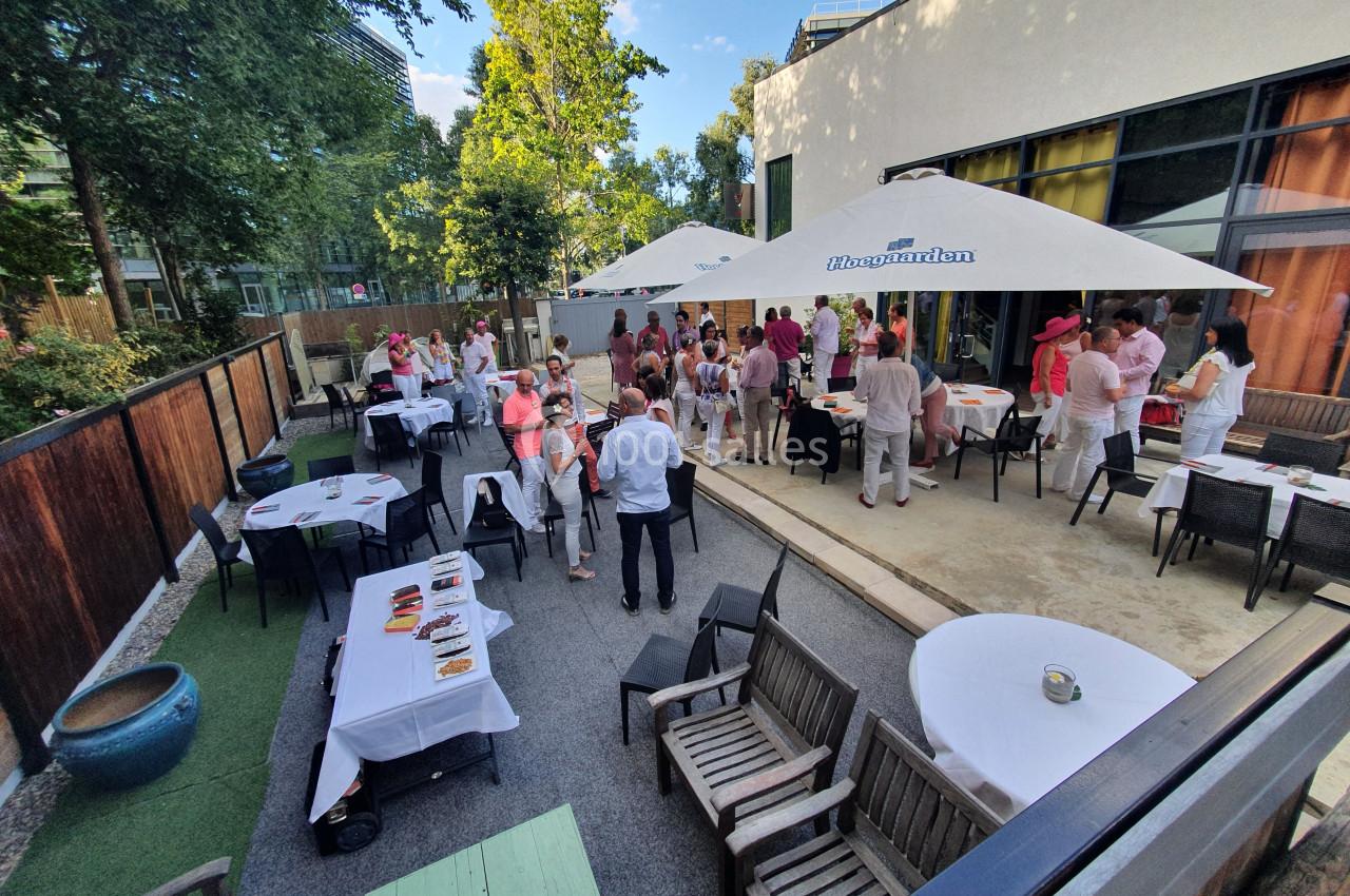 Groupe de personnes rassemblées dans une terrasse extérieure, avec tables dressées et parasols blancs.