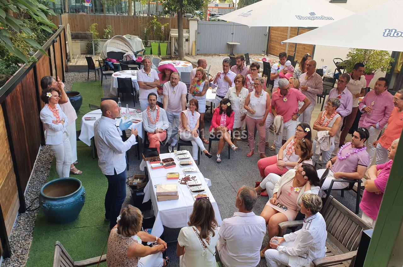 Un groupe de personnes assises et debout dans une cour extérieure, écoutant un homme qui fait une présentation.