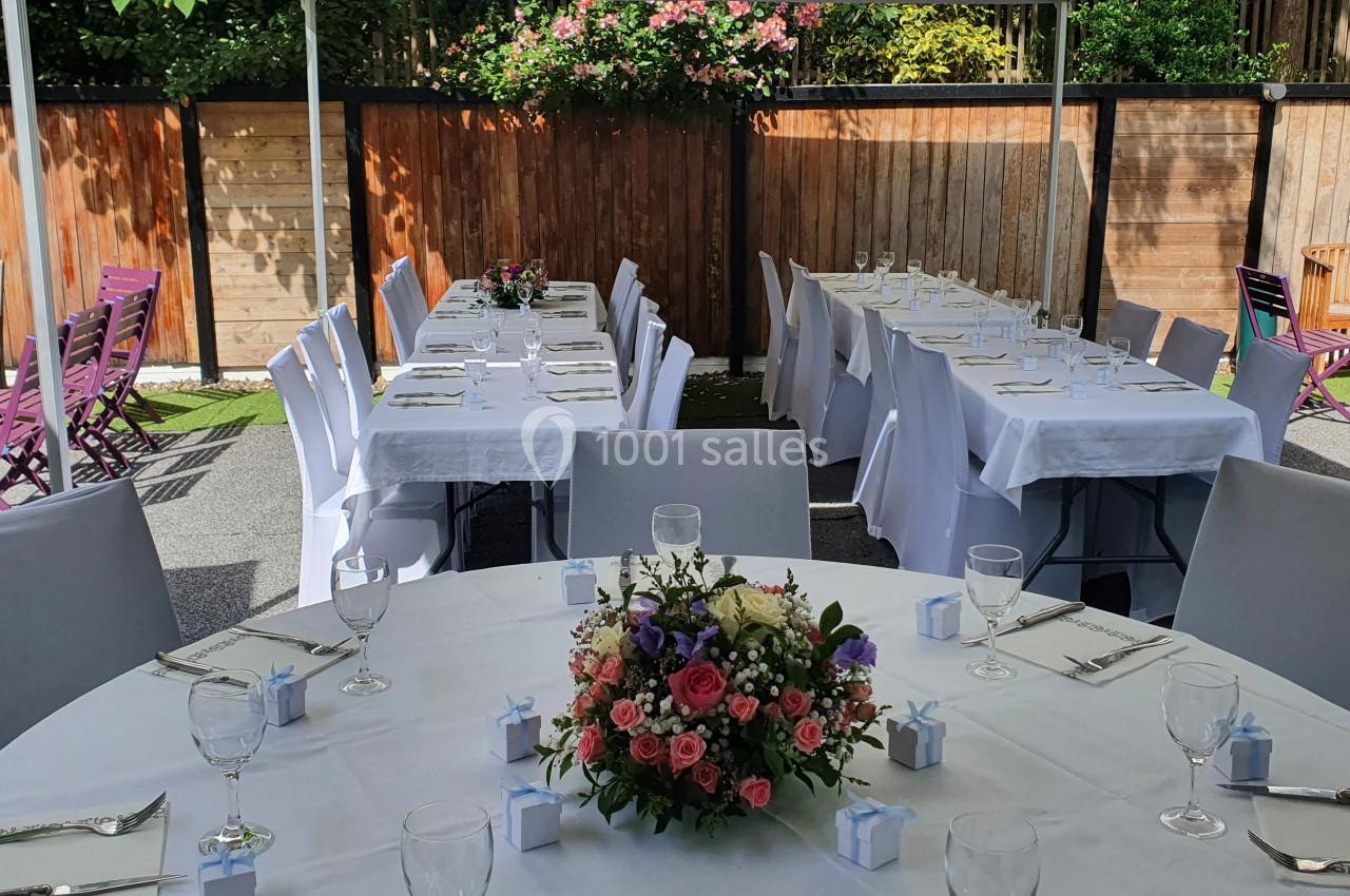 Tables dressées avec nappes blanches, décorées de fleurs et de petits cadeaux, sous une tente en extérieur.