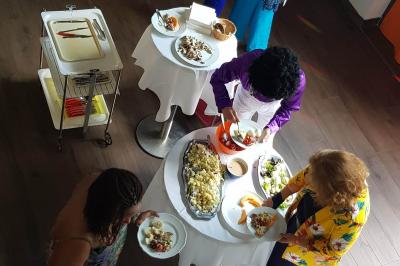 Buffet avec des plats variés, dont des salades, du saumon fumé et des fruits, décoré d'un bouquet de fleurs violettes et…