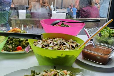 Buffet avec des plats variés, dont des salades, du saumon fumé et des fruits, décoré d'un bouquet de fleurs violettes et…