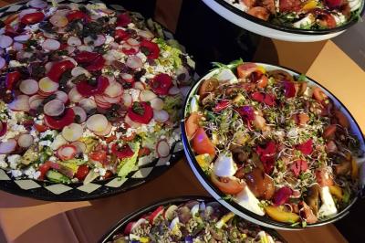 Buffet avec des plats variés, dont des salades, du saumon fumé et des fruits, décoré d'un bouquet de fleurs violettes et…