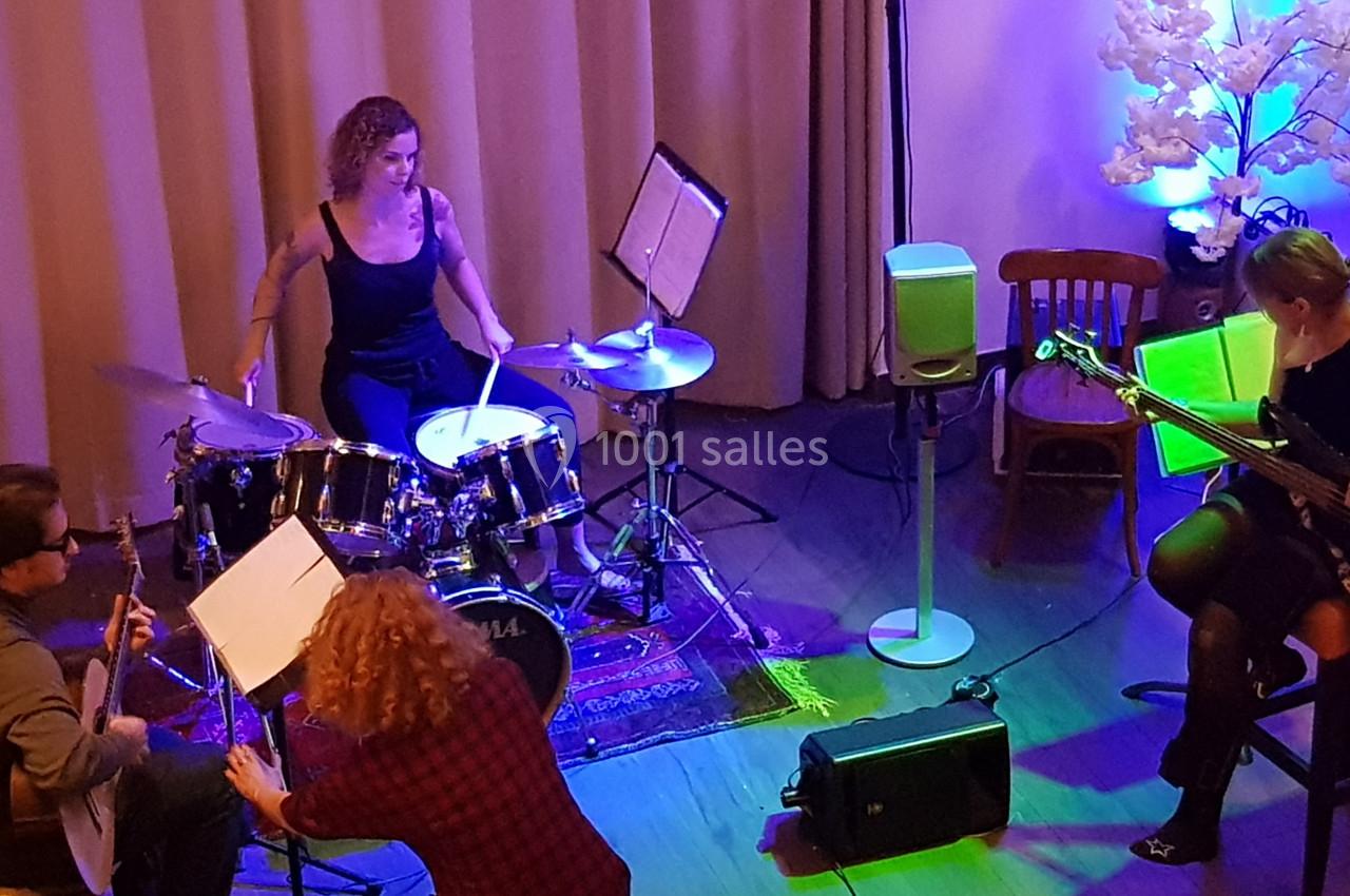 Un groupe de musiciens joue sur scène, avec une batteuse, une bassiste et deux guitaristes, dans une ambiance lumineuse.
