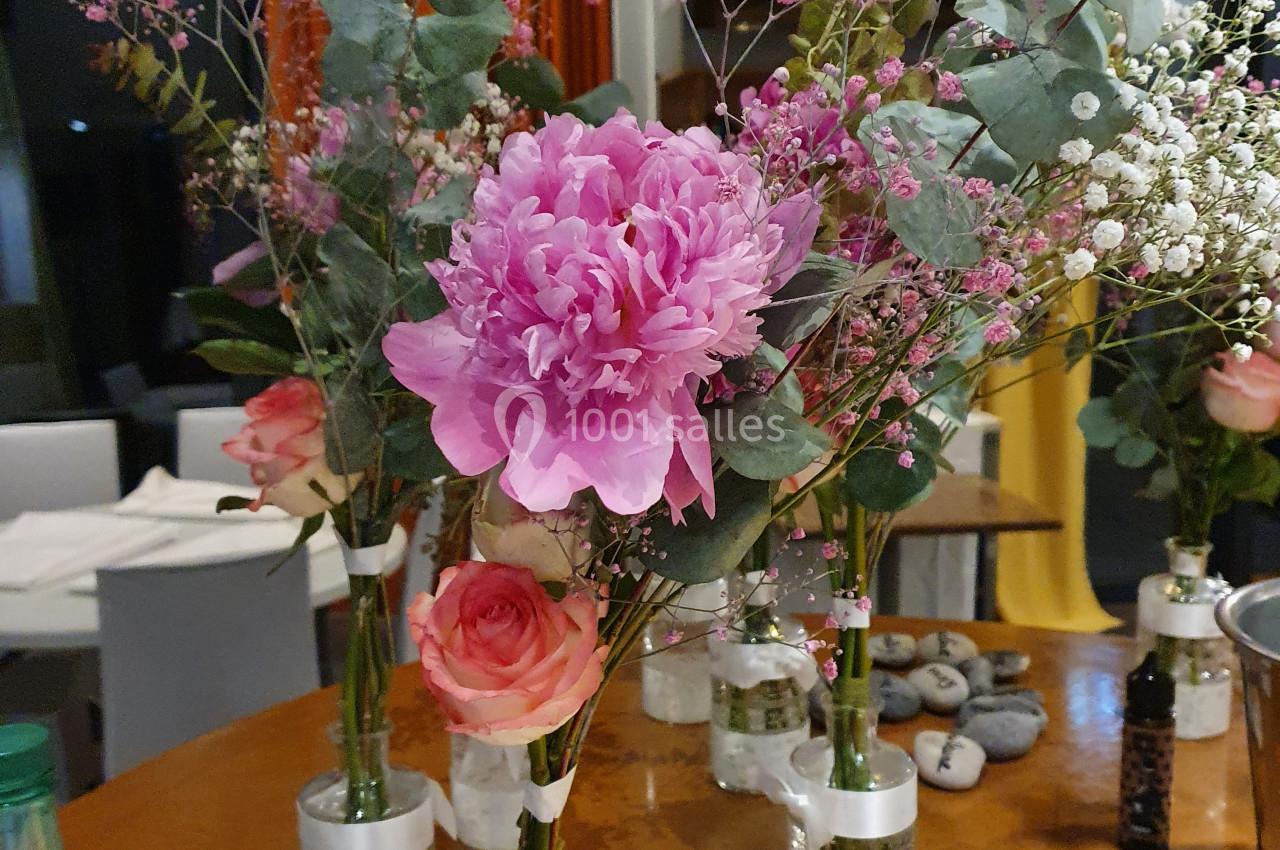 Bouquets de fleurs composés de pivoines roses, roses, gypsophiles et feuillages, disposés sur une table en bois.