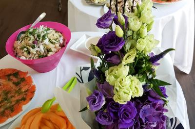Buffet avec des plats variés, dont des salades, du saumon fumé et des fruits, décoré d'un bouquet de fleurs violettes et…