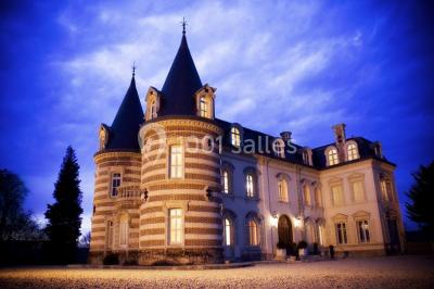 Vue nocturne d'une réception dans une tente éclairée, installée devant un bâtiment de style château.