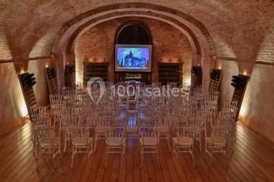 Vue nocturne d'une réception dans une tente éclairée, installée devant un bâtiment de style château.