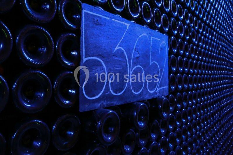 Des rangées de bouteilles en verre empilées dans une cave sombre, avec une ardoise portant le numéro 5362.