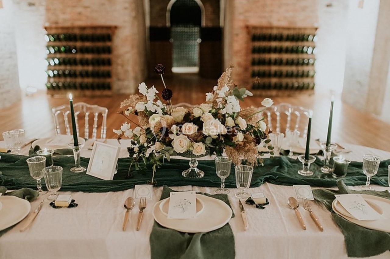 Table élégamment dressée avec nappes blanches et vertes, centre de table floral, vaisselle raffinée et bougies.