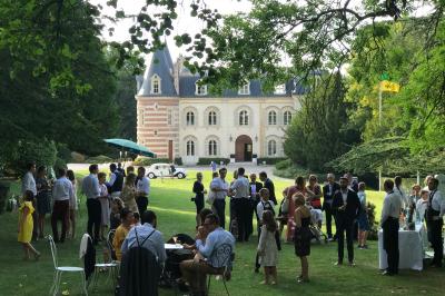 Vue nocturne d'une réception dans une tente éclairée, installée devant un bâtiment de style château.