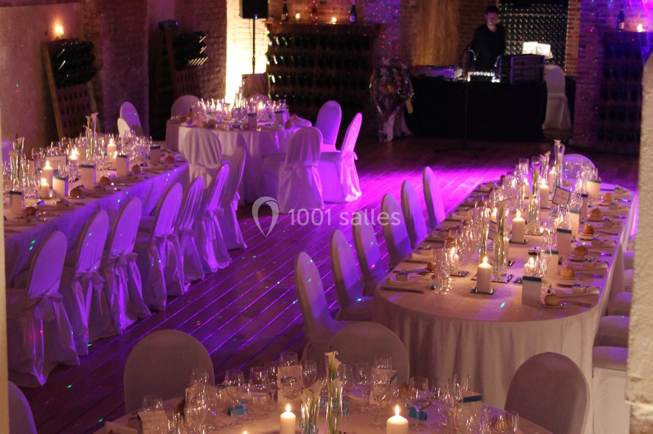 Salle voûtée en briques aménagée pour un dîner, avec tables rondes décorées et éclairage tamisé.