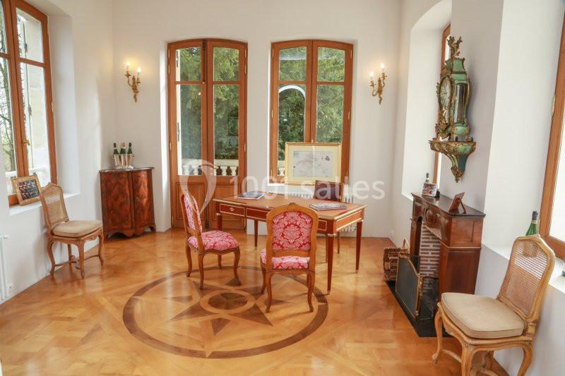 Bureau élégant avec parquet en bois, mobilier ancien, grandes fenêtres et vue sur un jardin verdoyant.
