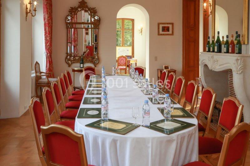 Salle élégante avec une grande table rectangulaire dressée, entourée de chaises rouges et décorée de bouteilles et miroirs.