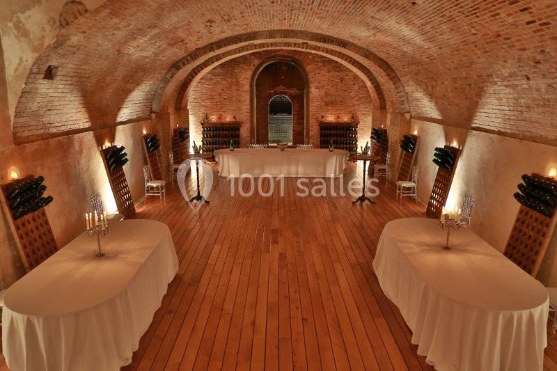 Salle voûtée en briques avec parquet en bois, tables dressées et éclairage tamisé.