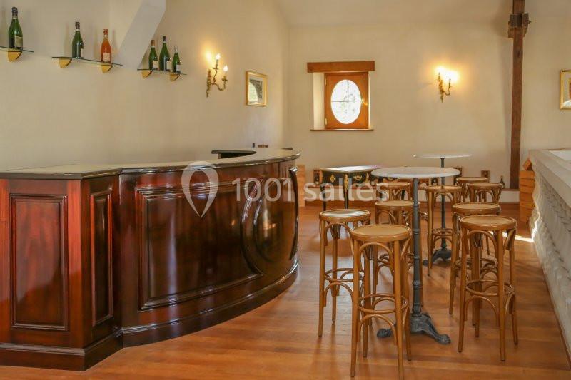 Bar en bois sombre avec tabourets et tables hautes dans une pièce lumineuse au sol en parquet.