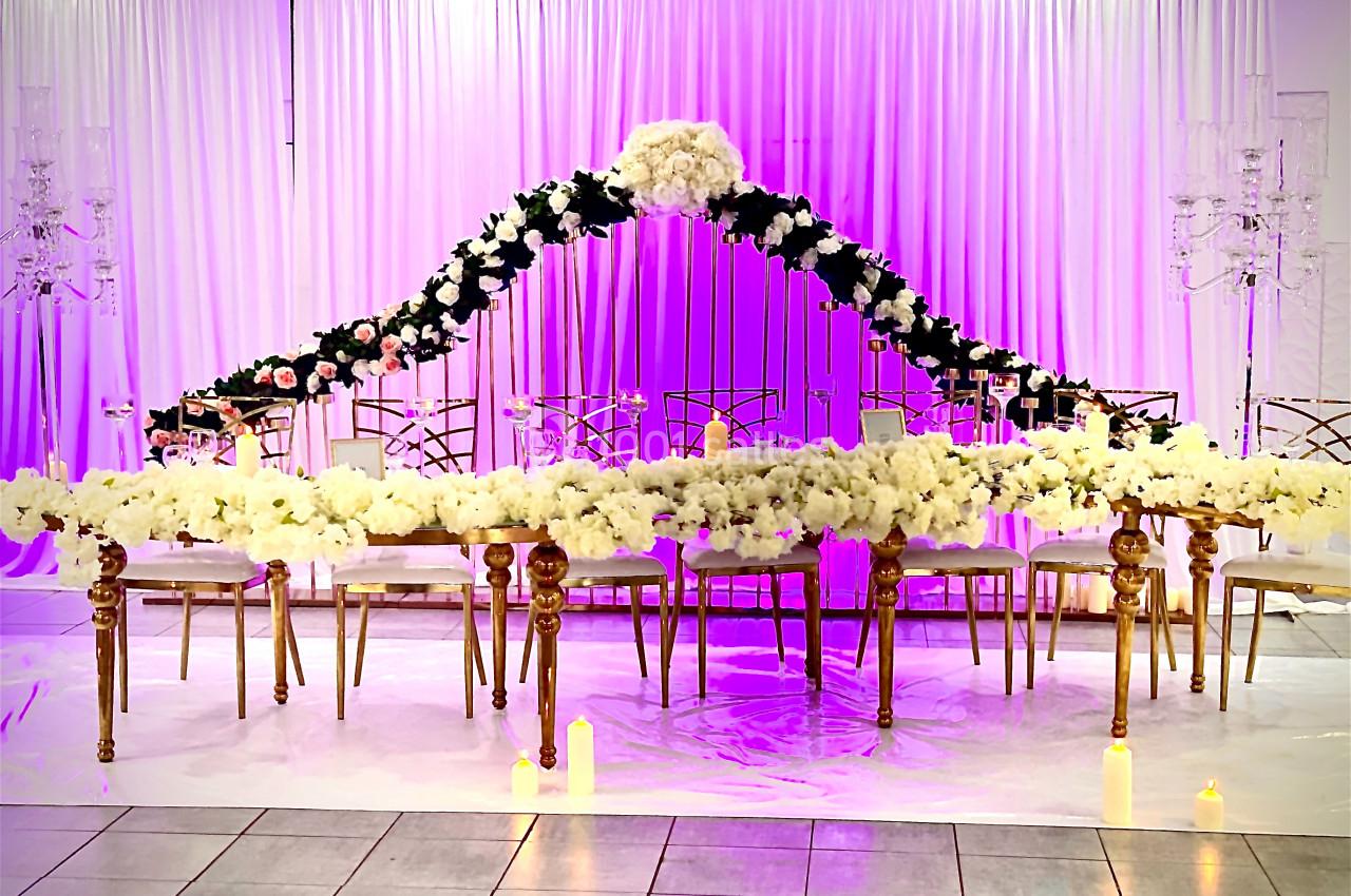 Table décorée pour un événement avec des fleurs blanches et noires, éclairage violet et rideaux en arrière-plan.