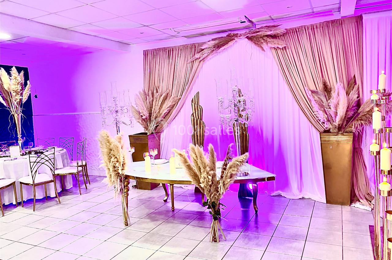 Salle de réception décorée avec des pampas, des rideaux roses et une table ornée d'éléments élégants.