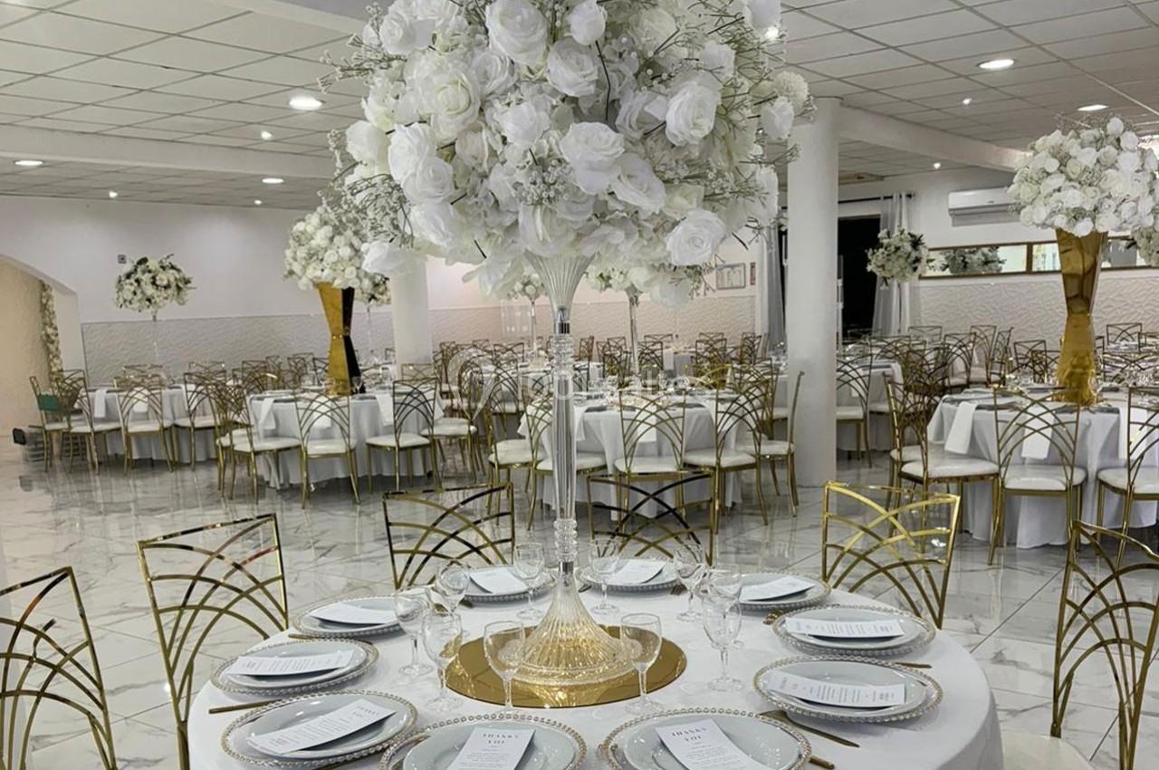 Salle de réception élégante avec tables décorées de nappes blanches, vaisselle raffinée et centres de table fleuris.