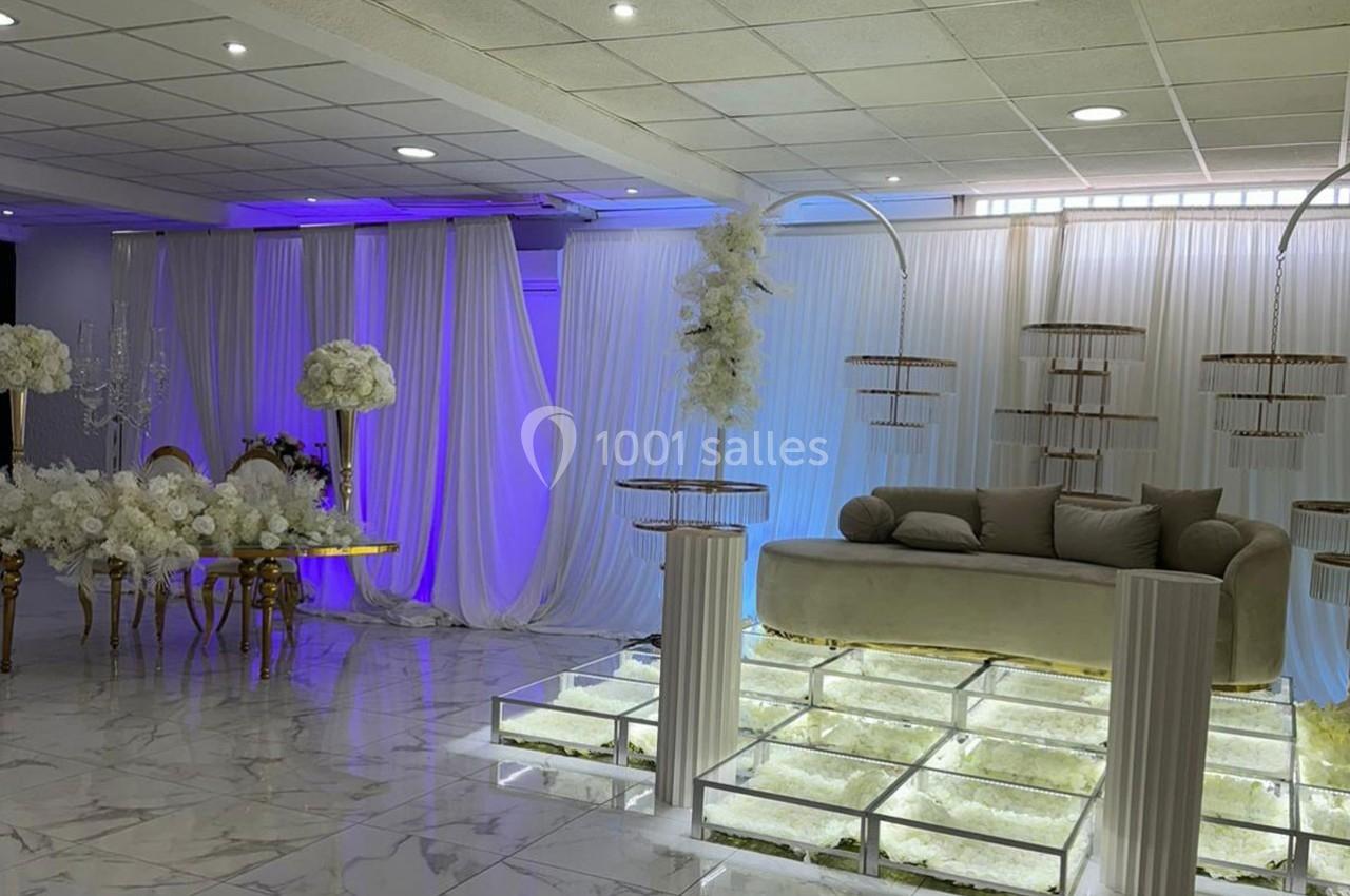 Salle de réception décorée avec des rideaux blancs, des fleurs, un canapé beige et un sol en verre illuminé.