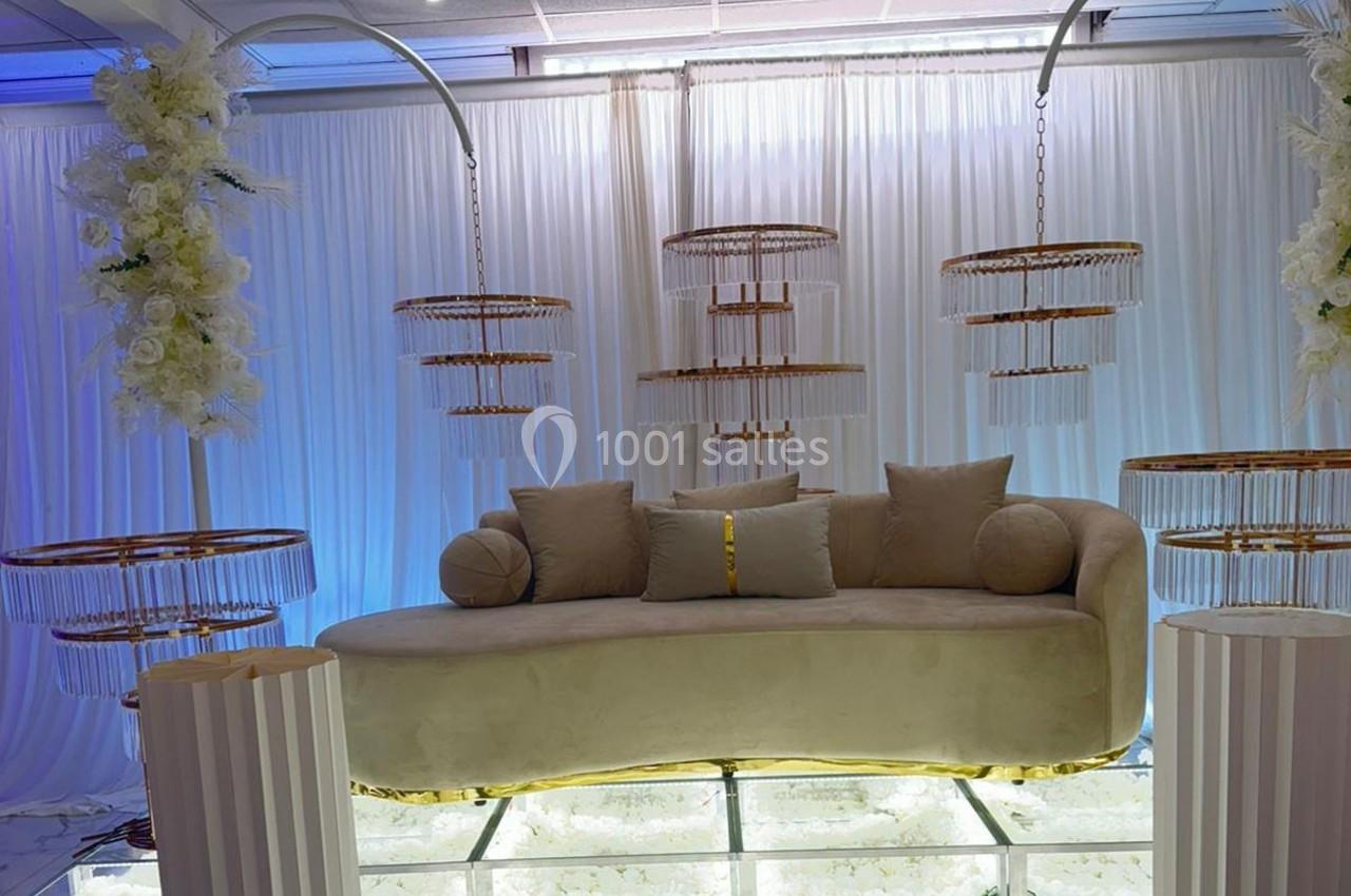 Canapé beige incurvé avec coussins, entouré de lustres suspendus et de colonnes décorées de fleurs blanches.