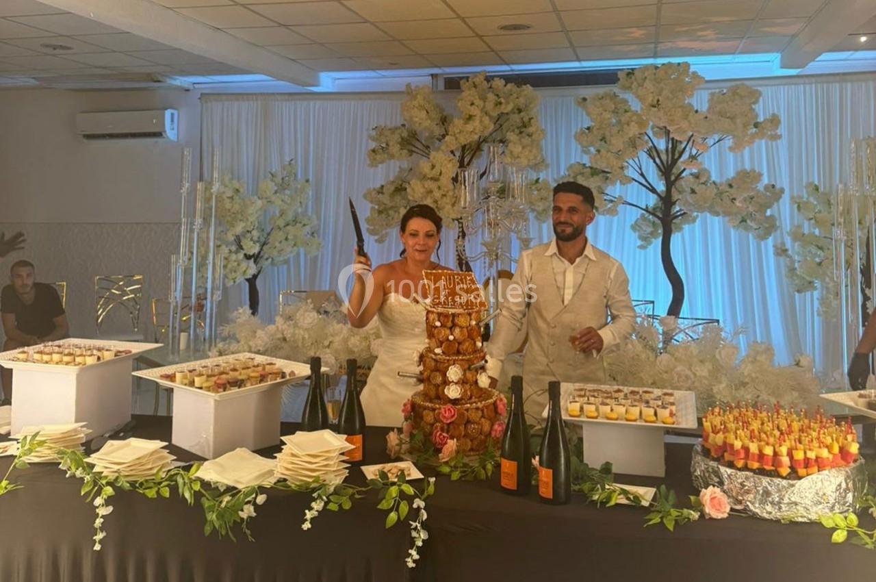 Un couple coupe une pièce montée lors d'une réception, entouré de desserts et d'une décoration florale.