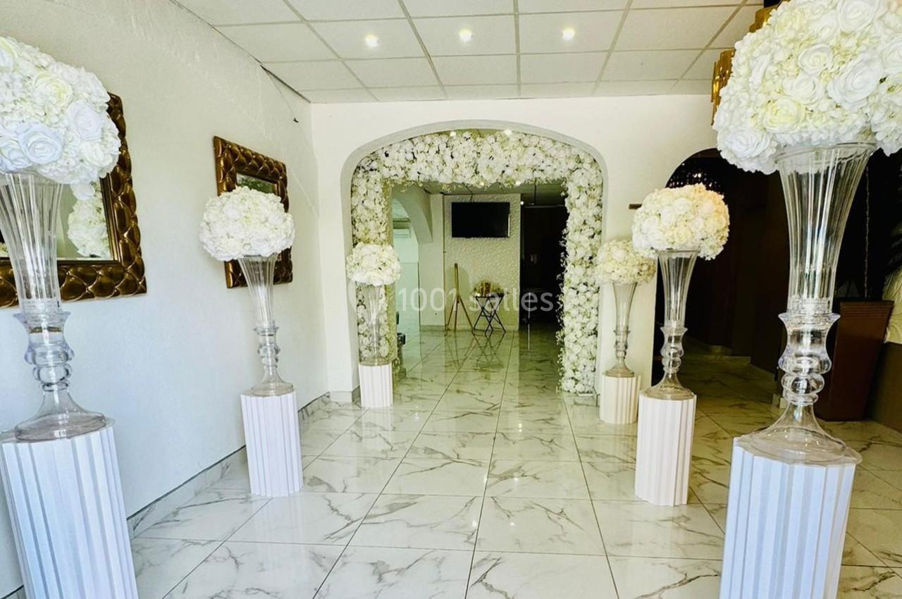 Salle décorée avec des arches et colonnes ornées de fleurs blanches, sol en marbre et miroirs muraux dorés.