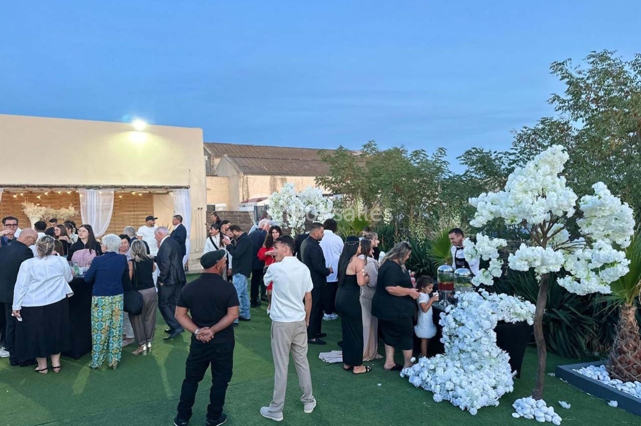 Groupe de personnes rassemblées dans un jardin en soirée, près de décorations florales blanches.