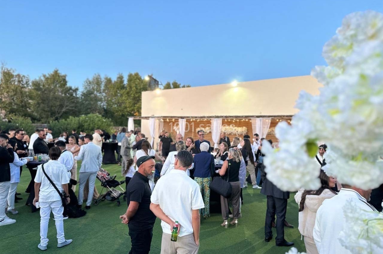 Groupe de personnes rassemblées en extérieur sur une pelouse, près d'un bâtiment éclairé, lors d'un événement en soirée.